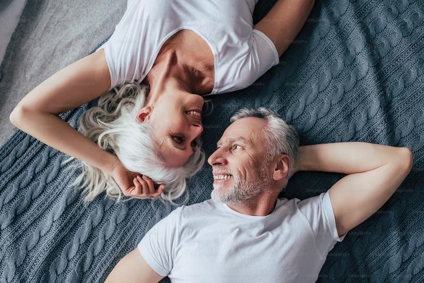 couple smiling at each other whilst laying on bed