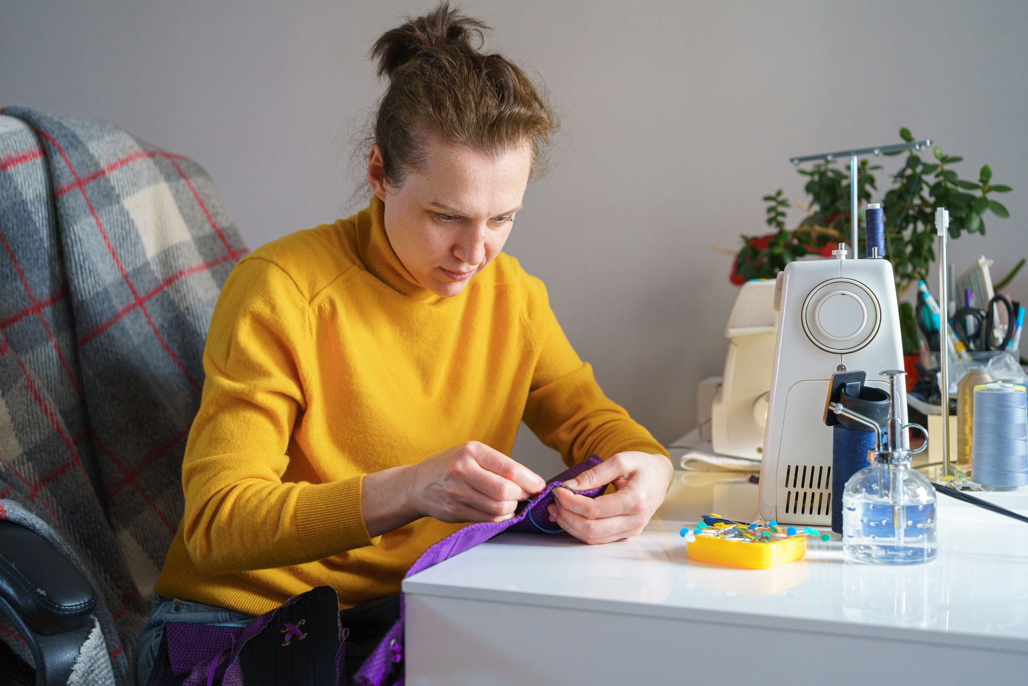Happy female seamstress looking at future garment while working remotely at her workspace at home
