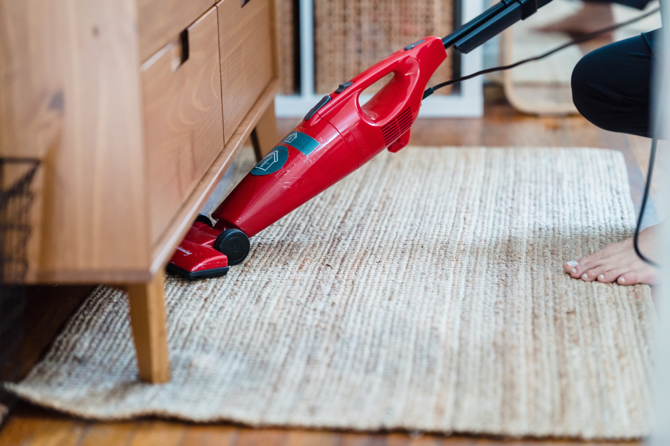 A-person-vacuuming-under-a-cabinet-scaled