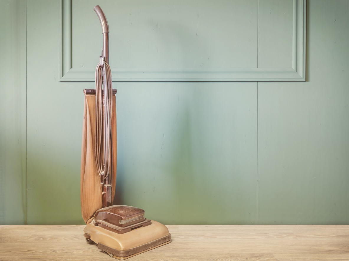 Vintage brown vacuum cleaner in an empty room with green wall and wooden floor