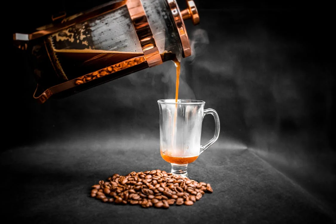 coffee being poured from French press into elegant glass