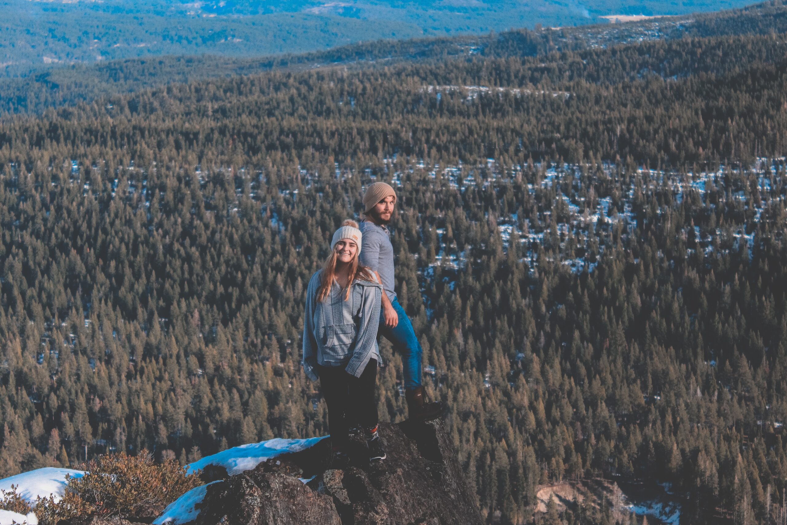 man and woman standing at the edge of a cliff near forest during day