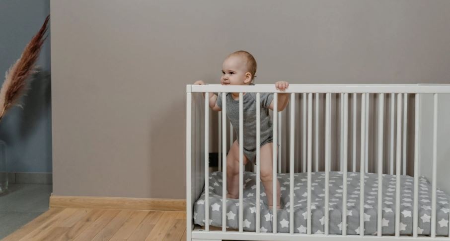 A-Baby-in-Gray-Baby-Onesie-Standing-in-a-Crib