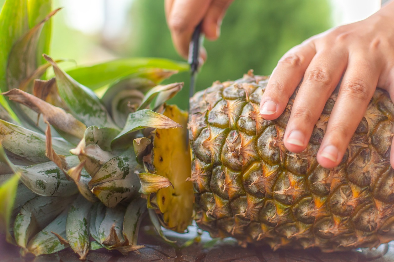 A-person-slicing-a-ripe-pineapple-with-a-sharp-knife-on-a-table