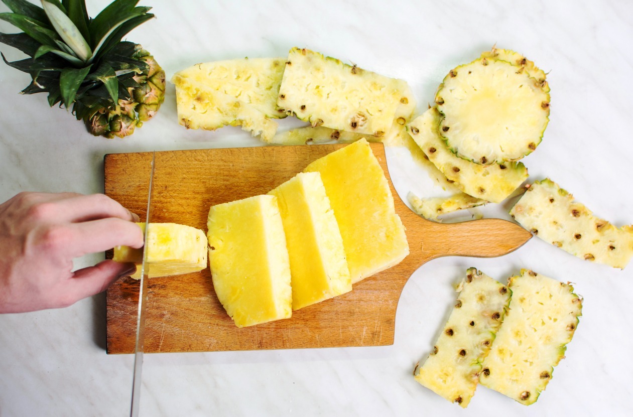 Male-hands-slicing-pineapple-fruit-on-a-wooden-board