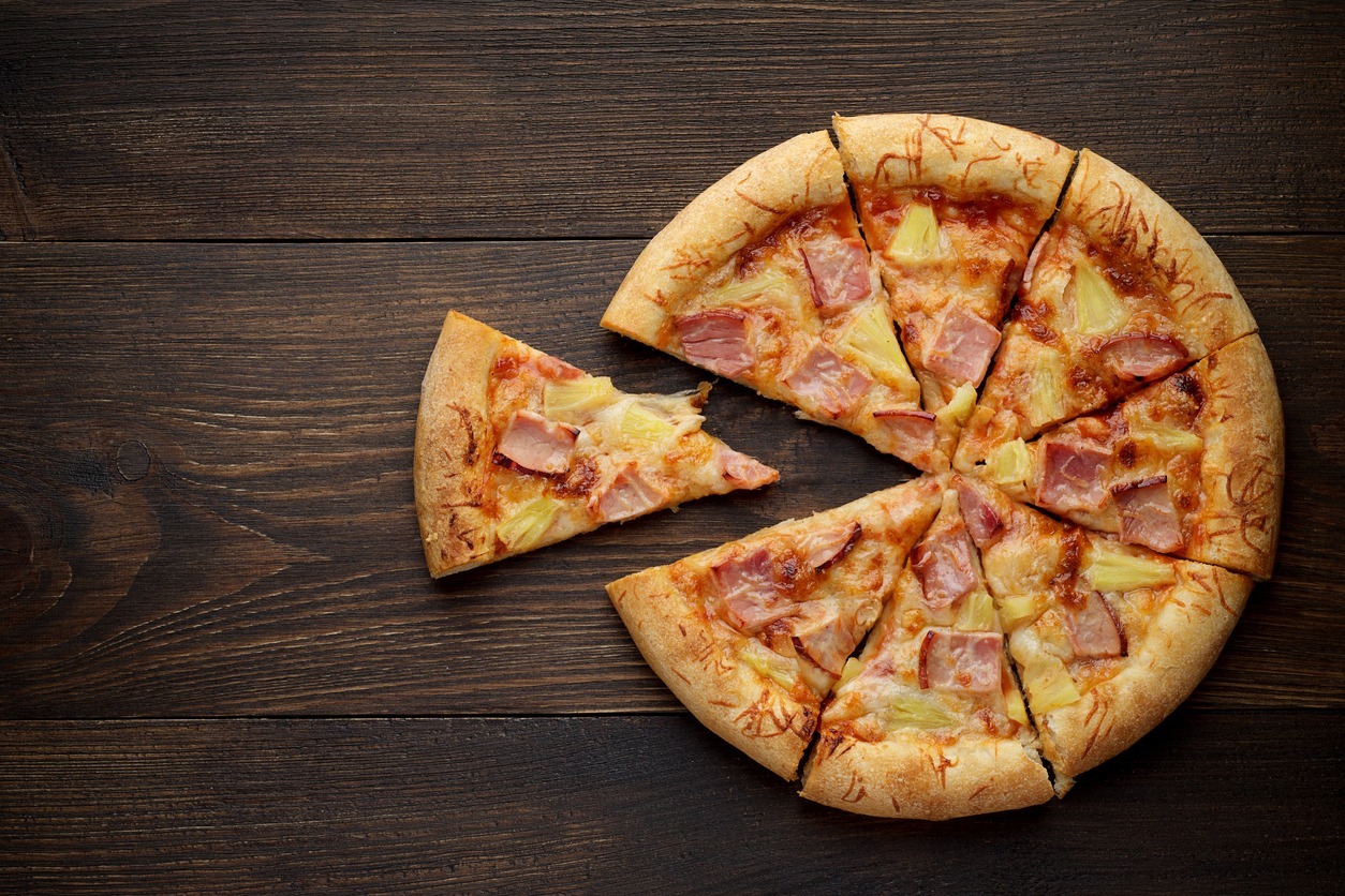 Sliced-Hawaiian-pizza-with-pineapple-and-ham-on-dark-rustic-wooden-background
