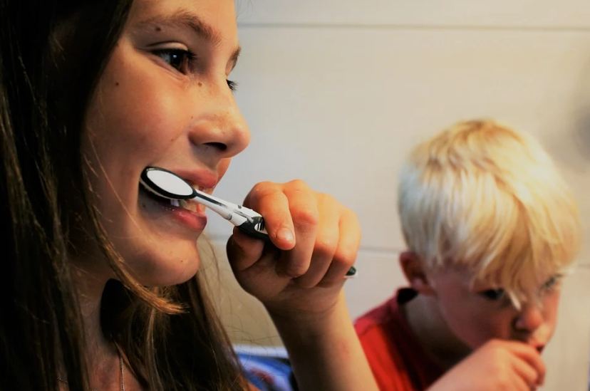 two-kids-brushing-their-teeth-girl-holding-a-black-and-white-toothbrush-boy-in-a-red-shirt