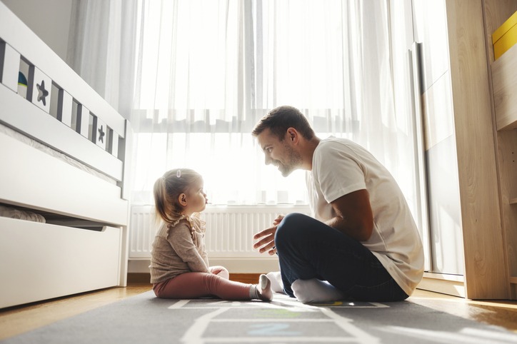 An angry daughter is sitting on the floor with her dad while he is teaching her good behavior